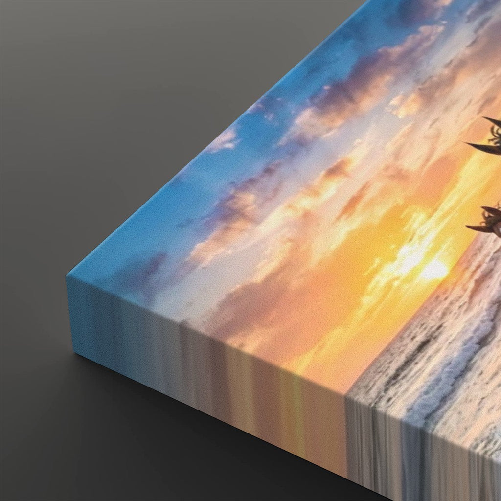 A rectangular canvas print showing a dramatic sunset over the ocean, photographed at an angle on a dark gray background. The artwork features a bright yellow and orange sun near the horizon, blue sky, and white sea foam, with the edge of the canvas visible on the left.