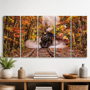 A five-panel canvas wall art set depicting an autumn forest scene with a steam train on tracks, displayed above a wooden console table with decorative vases, books, and a bowl in a styled interior setting.