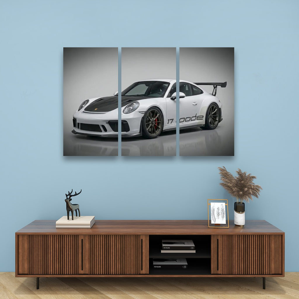 A three-panel canvas wall art print depicting a white Porsche 911 with black accents, displayed on a light blue wall above a wooden console table with decorative items.