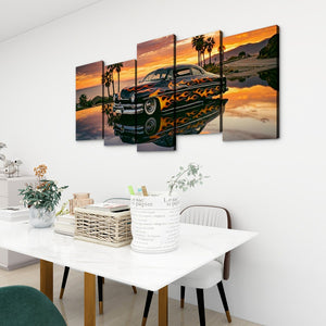 A 4-panel canvas wall art set depicting a classic car with flames on a beach at sunset, displayed on a white wall above a dining table in a modern room setting.