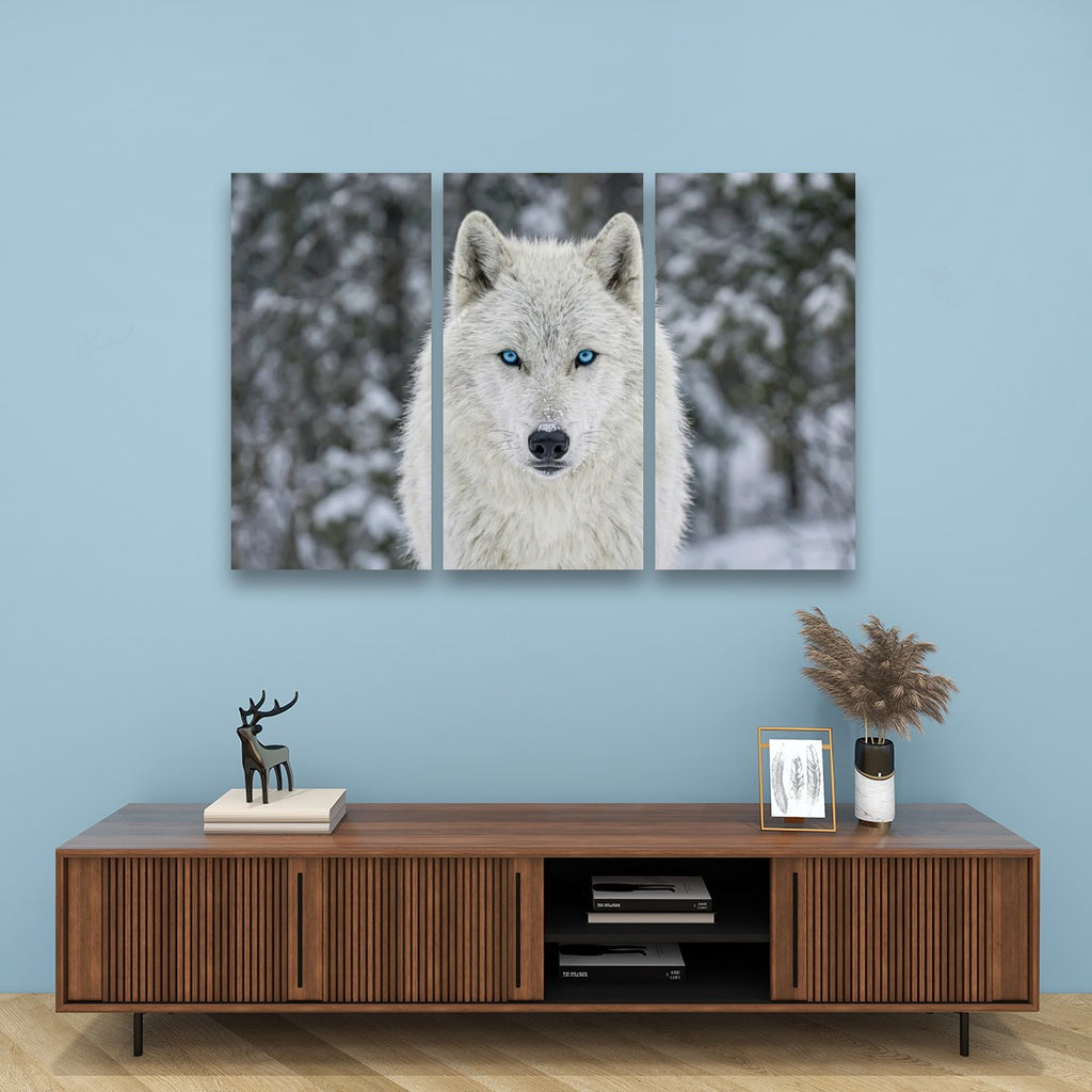 A three-panel canvas wall art set depicting a white wolf with blue eyes in a snowy winter setting, displayed on a light blue wall above a wooden console table with decorative items.