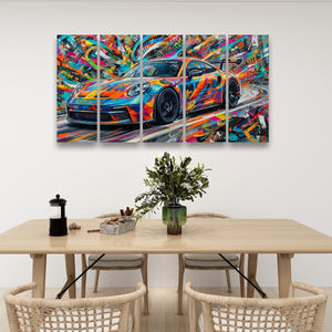A colorful abstract multi-panel canvas wall art print depicting a 911 GT3 sports car, displayed above a wooden dining table with chairs in a modern room setting.