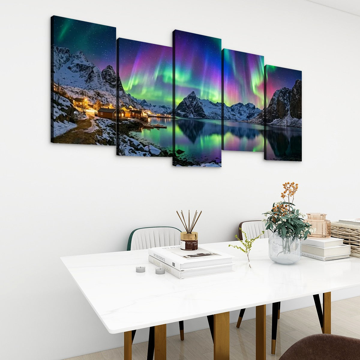 A 5-panel canvas wall art set depicting a scenic mountain lake landscape with glowing aurora borealis, displayed on a white wall above a modern dining table in a styled room.