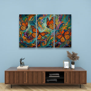 A three-panel canvas wall art set featuring vibrant orange monarch butterflies over colorful swirling abstract backgrounds, displayed on a light blue wall above a wooden console table with decorative items.
