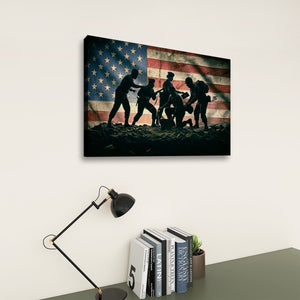 A rectangular wall art print hanging on a light wall above a desk, showing black silhouettes of soldiers carrying a wounded comrade in front of an American flag. The scene includes a black desk lamp, books, and a small plant below the artwork.