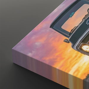 A close-up of a rectangular canvas or print showing part of a vintage car against a sunset sky, with pink, orange, and yellow tones. The product is photographed at an angle on a dark gray background.