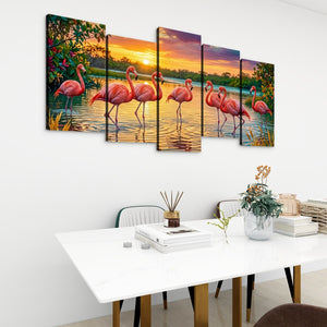 A five-panel canvas wall art set depicting pink flamingos standing in shallow water at sunset, displayed on a white wall above a dining table in a modern room setting.