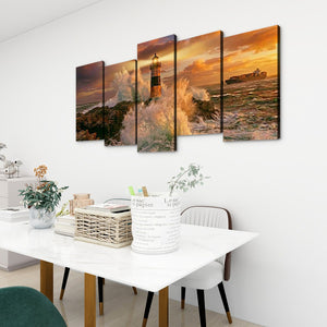 A 4-panel canvas wall art set depicting a dramatic lighthouse and rocky coastline at sunset, displayed on a white wall above a dining table in a modern room setting.