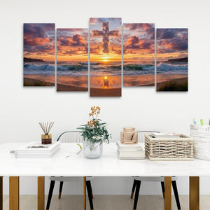 A five-panel canvas wall art set depicting a dramatic sunset over the ocean waves and sandy beach, displayed on a white wall above a modern dining table with books, a vase, and baskets.