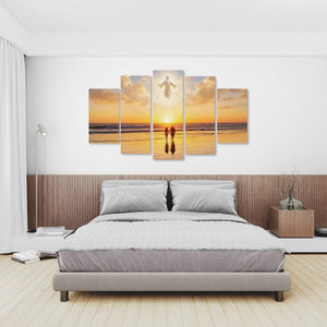 A 5-panel canvas wall art set depicting a sunset beach scene with a glowing angel figure, displayed above a bed in a modern, neutral-toned bedroom.