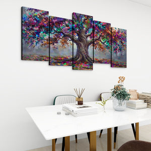 A 5-panel canvas wall art set depicting a colorful, painterly tree with a gnarled trunk, displayed on a white wall above a modern white dining table with books and a vase.