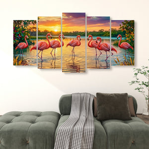 A five-panel canvas wall art set depicting pink flamingos standing in a lake at sunset, displayed above a green sofa in a living room setting.