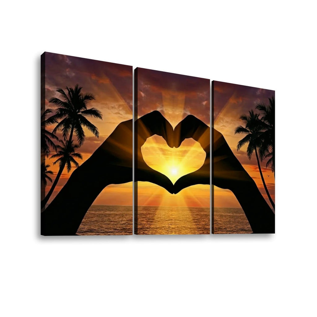 Three-panel canvas wall art showing a sunset seascape with palm trees and two silhouetted hands forming a heart shape over the ocean.