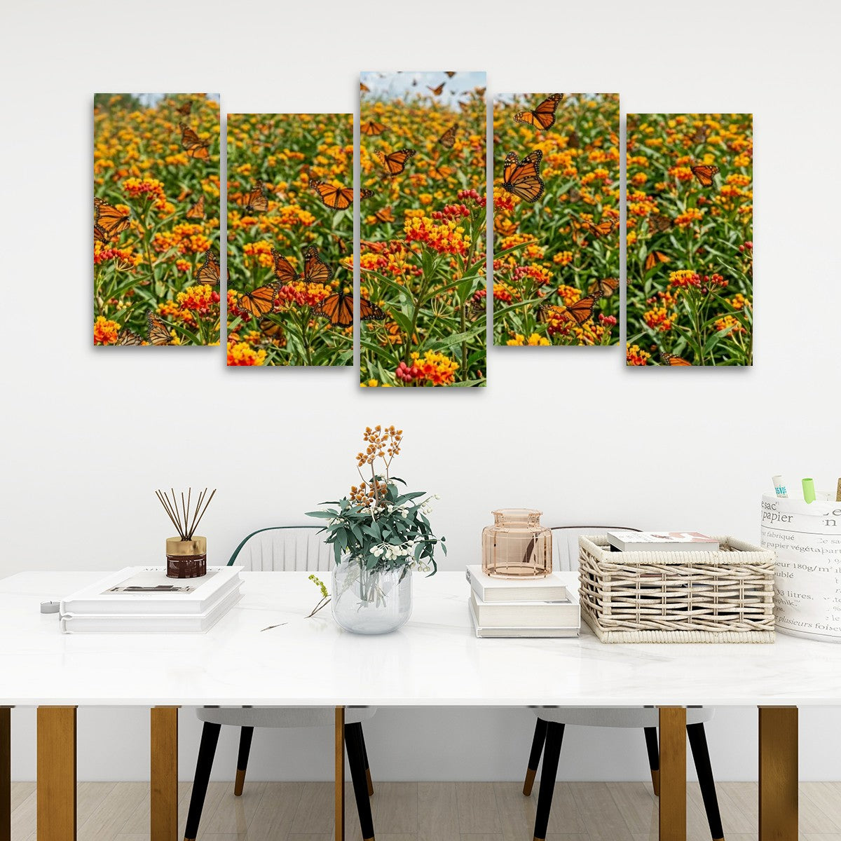 A five-panel canvas wall art set depicting a vibrant field of orange and yellow flowers with monarch butterflies, displayed on a white wall above a styled dining table.
