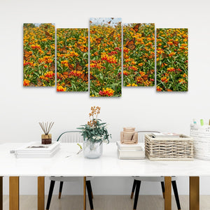 A five-panel canvas wall art set depicting a vibrant field of orange and yellow flowers with monarch butterflies, displayed on a white wall above a styled dining table.