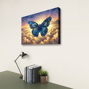 A rectangular wall art canvas showing a large blue butterfly over glowing clouds, displayed on a light wall above a desk with a lamp, books, and a small plant.