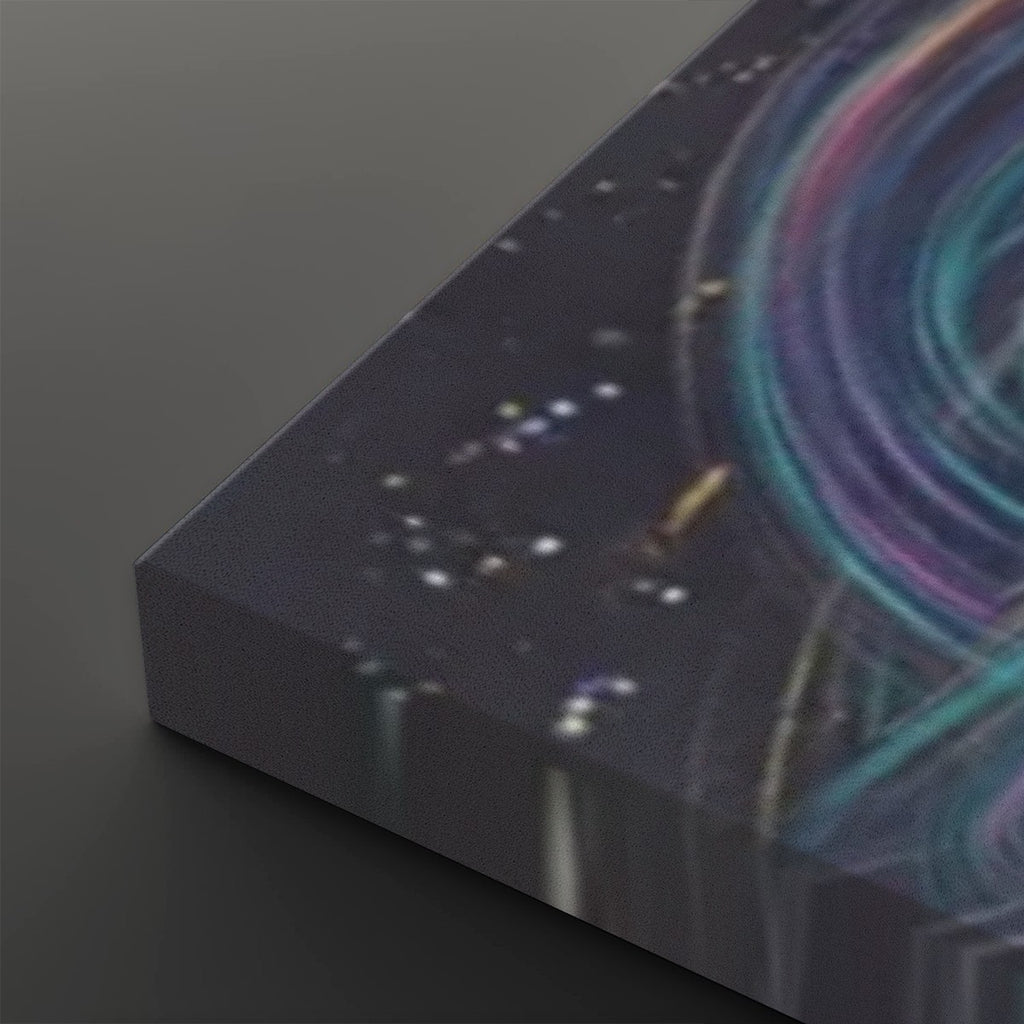 A close-up of a rectangular canvas or print showing an abstract cosmic scene with a dark starry background and swirling teal, purple, and pink light trails, photographed on a dark gray surface.