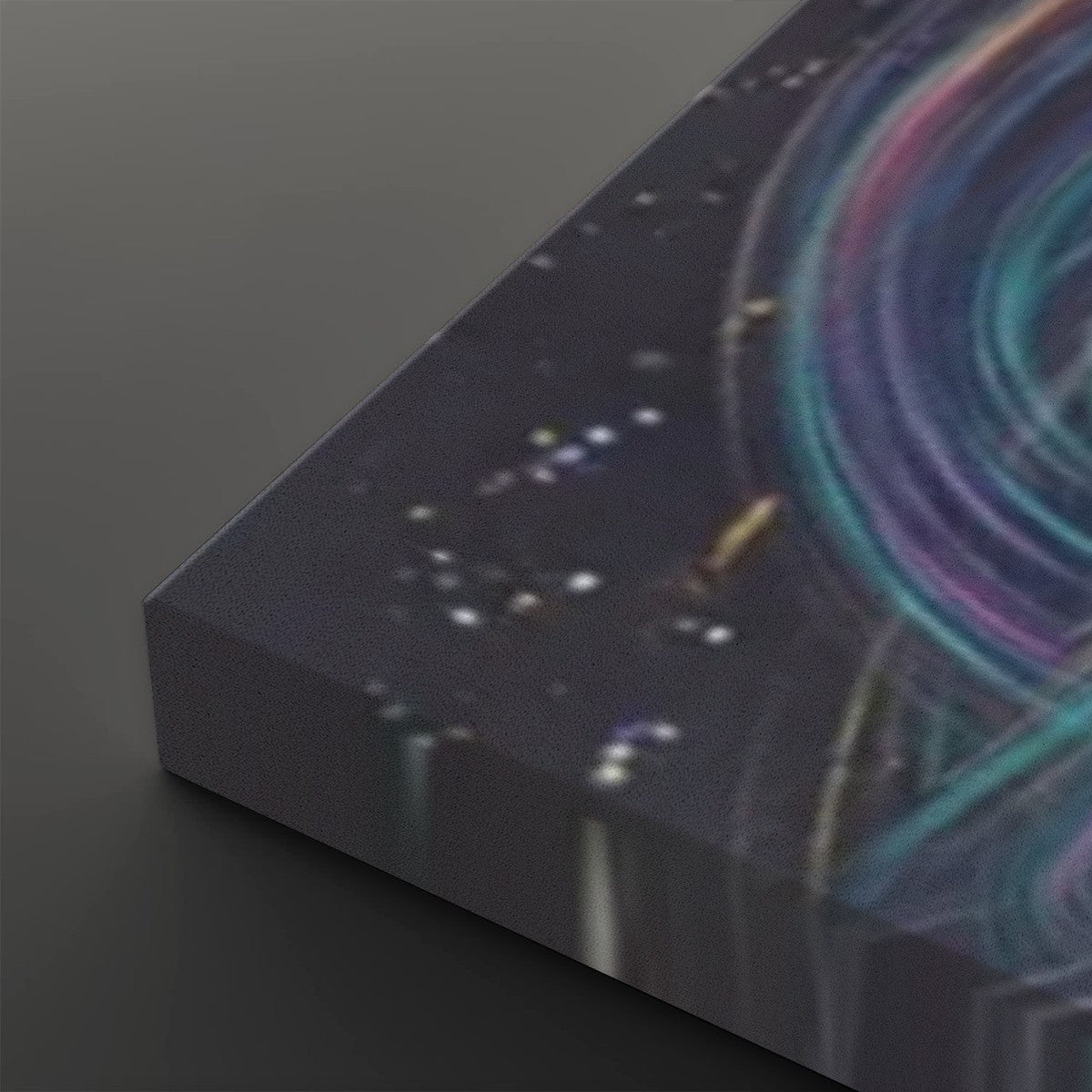 A close-up of a rectangular canvas or print showing an abstract cosmic scene with a dark starry background and swirling teal, purple, and pink light trails, photographed on a dark gray surface.