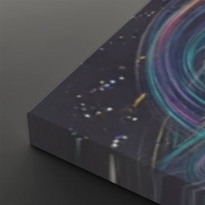A close-up of a rectangular canvas or print showing an abstract cosmic scene with a dark starry background and swirling teal, purple, and pink light trails, photographed on a dark gray surface.