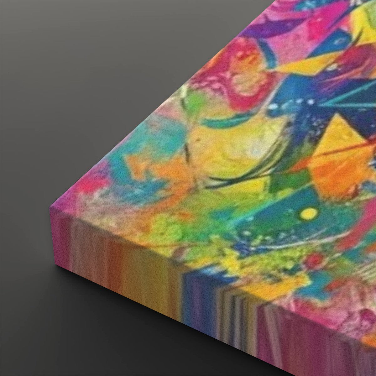 A close-up angled view of a colorful abstract canvas print showing vivid brushstrokes and splashes of pink, yellow, blue, green, orange, and purple on a dark gray background.