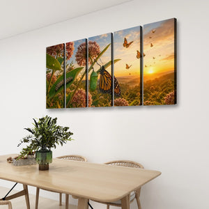 A four-panel canvas wall art set depicting monarch butterflies, green caterpillars, and wildflowers at sunset, displayed on a white wall above a light wood dining table with chairs and a potted plant.