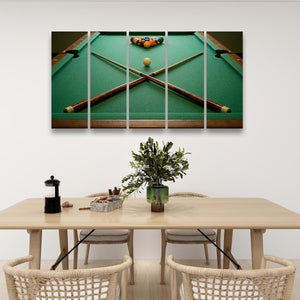 A four-panel canvas wall art print depicting a green pool table with crossed pool cues and a triangle rack of billiard balls, displayed above a light wood dining table with woven chairs in a modern room setting.