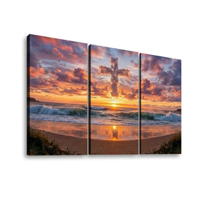 Three-panel canvas wall art showing a beach sunset with orange and pink clouds, ocean waves, and sand reflections, displayed against a light gray background.