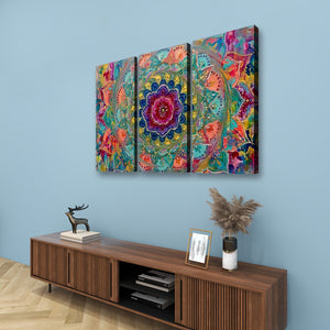 A three-panel canvas wall art set featuring a vibrant, colorful mandala and floral design, displayed on a light blue wall above a wooden console table.