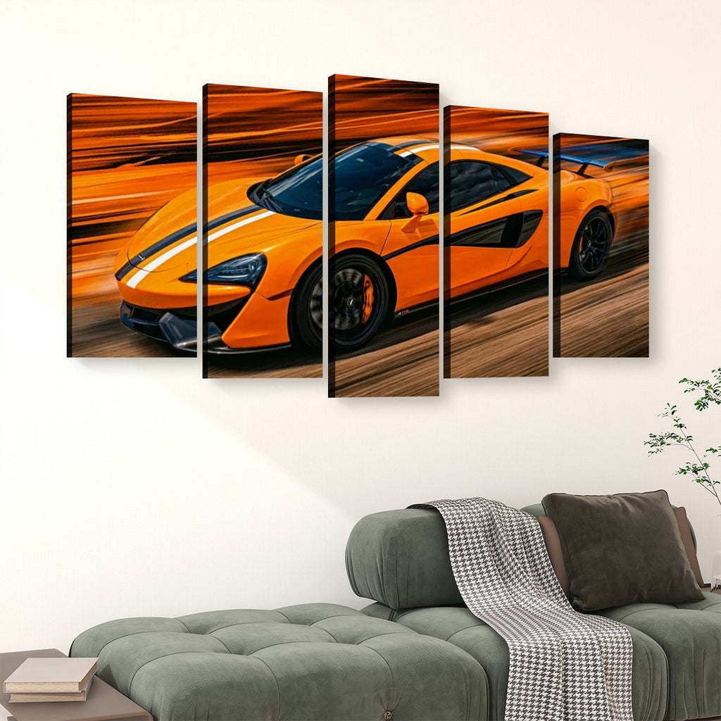 A five-panel canvas wall art set depicting a bright orange sports car with black racing stripes on a blurred orange and brown background, displayed above a green sofa in a living room setting.