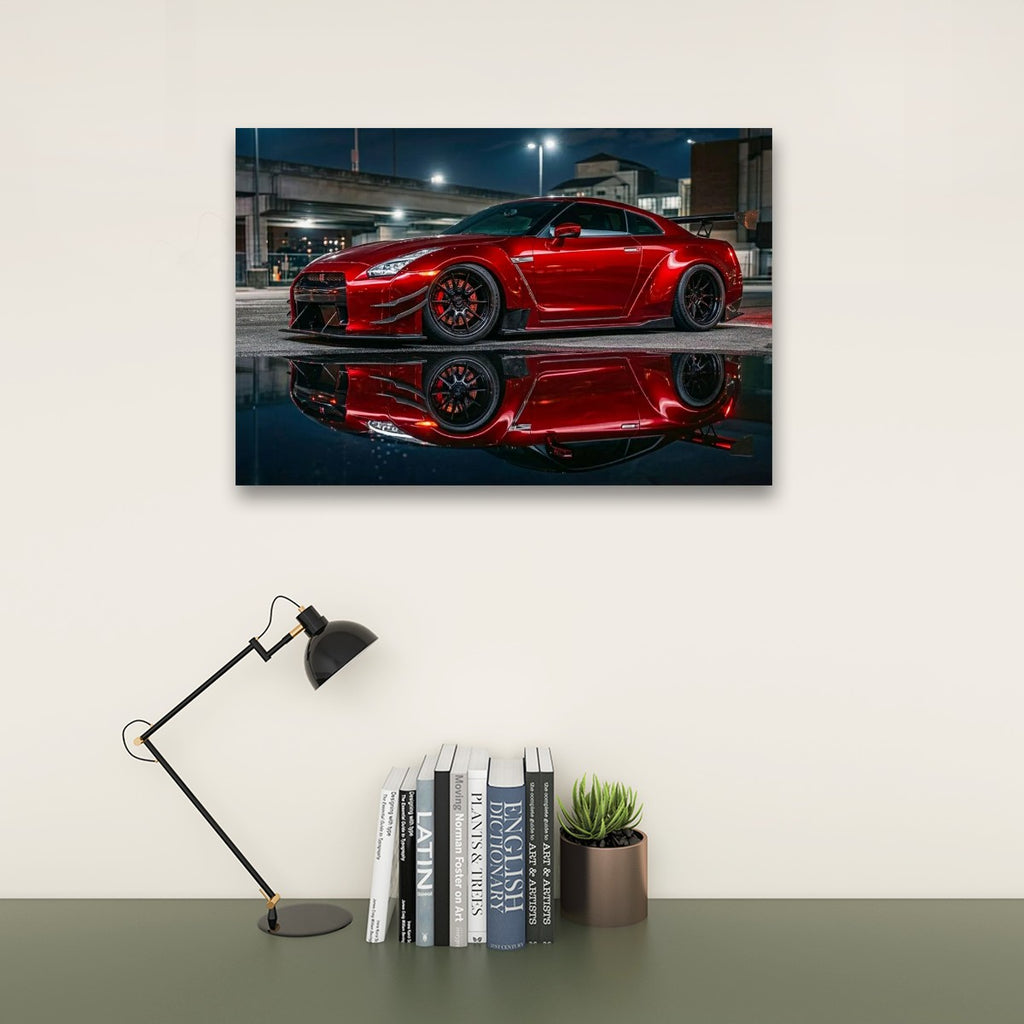 A framed wall art print showing a red  Nissan GTR R35  sports car reflected in dark water, displayed above a desk with a black lamp, books, and a small succulent in a styled interior setting.