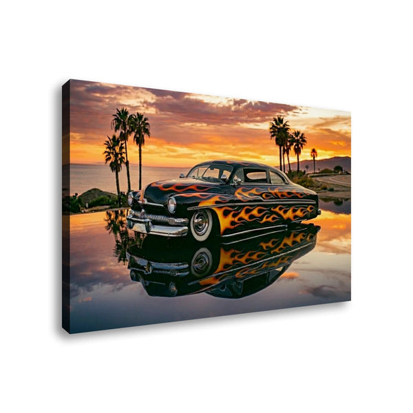 A rectangular canvas wall art print showing a black vintage car with orange and yellow flame decals, parked on reflective water at sunset with palm trees and a warm sky in the background.