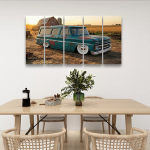 A five-panel canvas wall art print depicting a vintage teal 1966 Chevy Suburban Carryall station wagon parked in a rural field at sunset, displayed above a light wood dining table with woven chairs in a modern dining room setting.