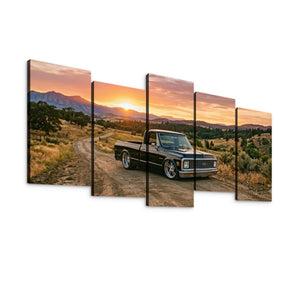 A five-panel canvas wall art set depicting a black 1970 Chevy C10 Fleetside pickup truck parked on a dirt road at sunset, with mountains and grassy hills in the background, shown against a plain white wall.