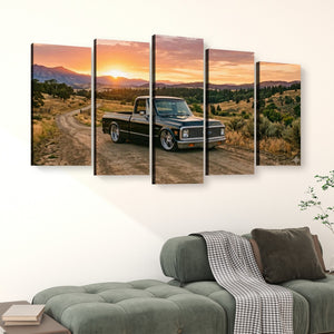 A five-panel canvas wall art set depicting a black vintage 1970 Chevy C10 Fleetside pickup truck on a dirt road at sunset, displayed above a green sofa in a living room setting.