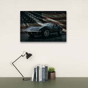 A framed wall art print showing a dark 1972 Corvette sports car in front of a distressed American flag, displayed above a desk with a black lamp, books, and a small succulent in a styled interior setting.
