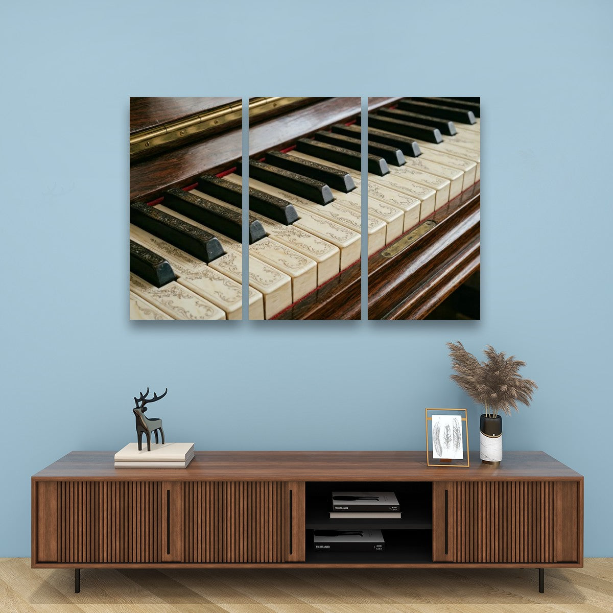 A three-panel canvas wall art print depicting a close-up of vintage piano keys, displayed on a light blue wall above a wooden console table with decorative items.