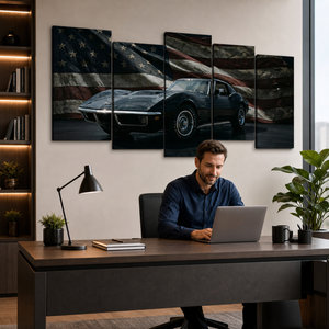 A man sits at a desk using a laptop in a modern home office, with a five-panel canvas wall art set hanging above him. The artwork shows a black sports car against a distressed American flag background.