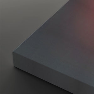 A close-up of a matte gray rectangular block or panel corner, shown against a matching dark gray background with a soft warm red glow in the upper right.