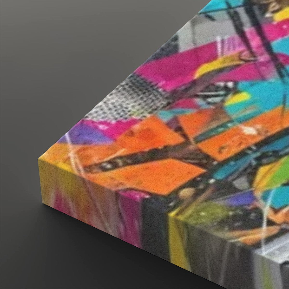 A close-up angled view of a colorful abstract canvas print showing vibrant brushstrokes and geometric shapes in pink, orange, yellow, blue, black, and white on a dark gray background.