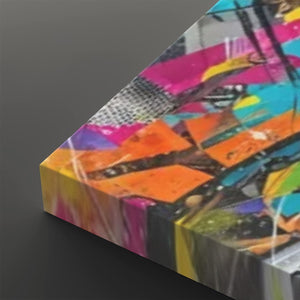 A close-up angled view of a colorful abstract canvas print showing vibrant brushstrokes and geometric shapes in pink, orange, yellow, blue, black, and white on a dark gray background.