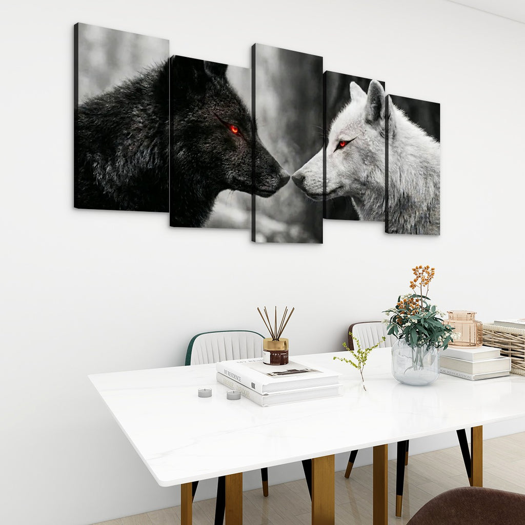 Five-panel canvas wall art depicting a black wolf and a white wolf facing each other, displayed on a white wall above a dining table in a modern room setting.