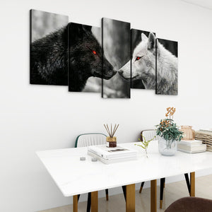 Five-panel canvas wall art depicting a black wolf and a white wolf facing each other, displayed on a white wall above a dining table in a modern room setting.