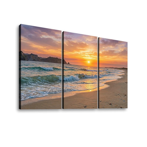 Three-panel canvas wall art showing a beach sunset with ocean waves, sandy shore, and dramatic clouds, displayed against a light gray background.