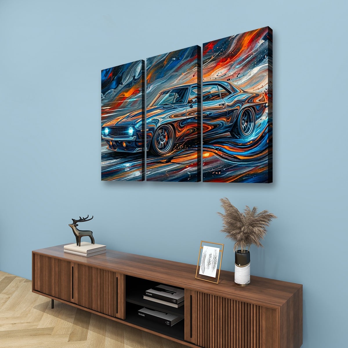 A three-panel canvas wall art set depicting a stylized blue 1969  Camaro  sports car with swirling orange, red, white, and black brushstrokes, displayed above a wooden console table against a light blue wall.