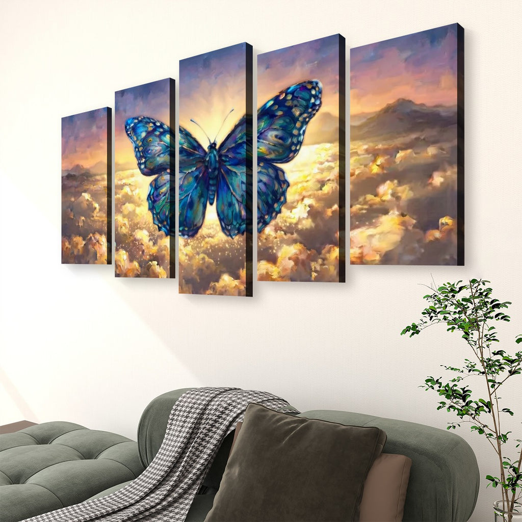 A 4-panel canvas wall art set depicting a large blue butterfly over a dramatic sky with golden clouds and distant mountains, displayed above a green sofa in a living room setting.