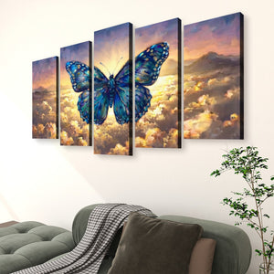 A 4-panel canvas wall art set depicting a large blue butterfly over a dramatic sky with golden clouds and distant mountains, displayed above a green sofa in a living room setting.