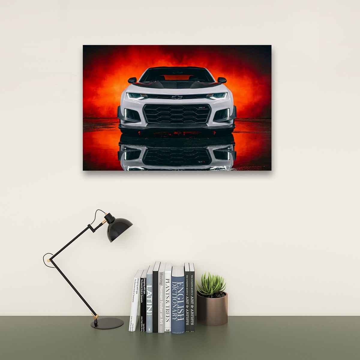 A rectangular wall art print showing a white sports car against a vivid red and orange smoky background, displayed above a desk with a black lamp, books, and a small plant in a styled interior.
