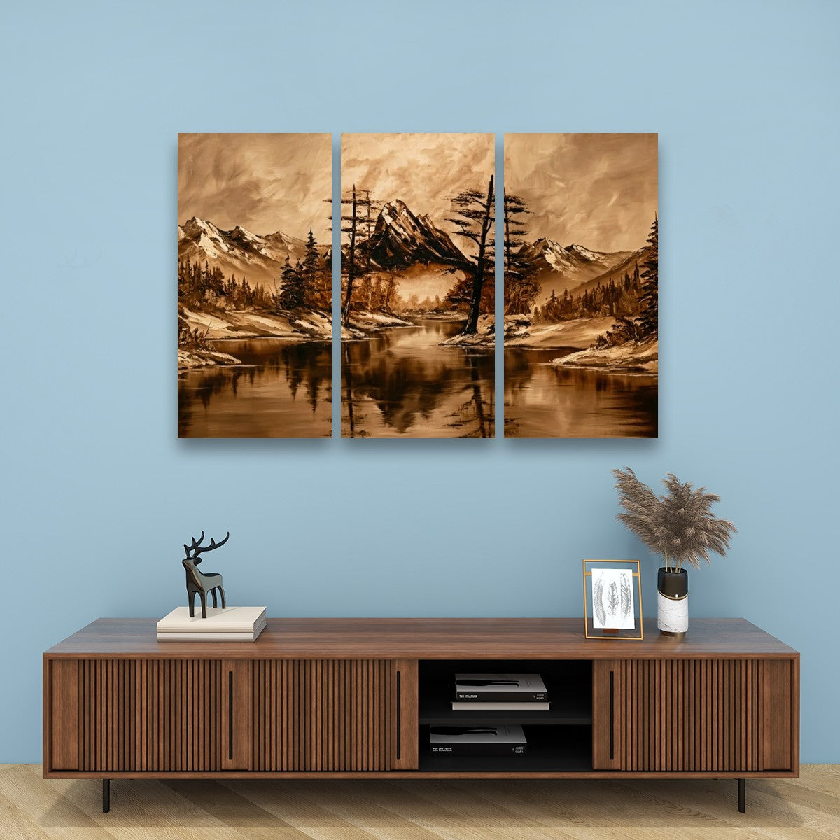 A three-panel canvas wall art set depicting a sepia-toned mountain lake landscape with trees and reflections, displayed above a wooden console table against a light blue wall.