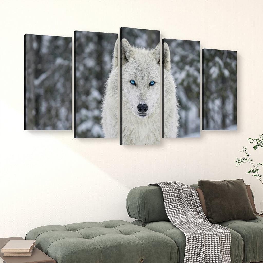A five-panel canvas wall art set depicting a white wolf with bright blue eyes in a snowy forest, displayed above a green sofa in a living room setting.