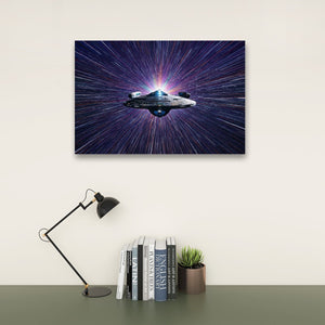 A rectangular wall art print showing a spaceship against a starburst space background, displayed above a desk with books, a small plant, and a black desk lamp in a styled interior setting.